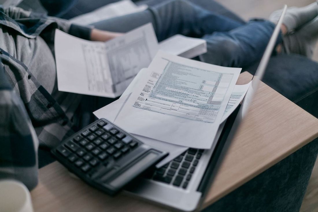Handen met rekenmachine en documenten naast een laptop